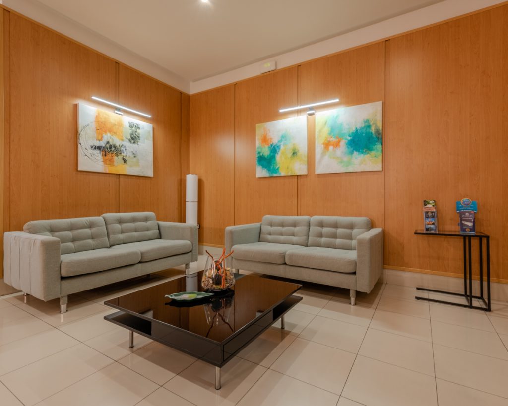 Área de descanso con sofás grises y obras de arte coloridas en las paredes de un hotel.
