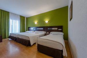 Habitación de hotel con camas individuales, pared verde y decoración moderna.